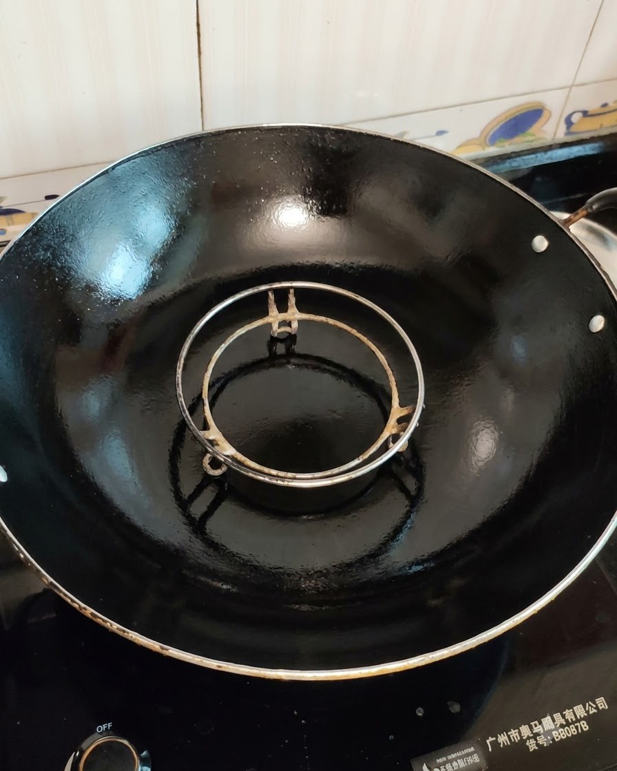 大きな黒い中華鍋の中にセットされた、調理前の空の蒸し器ラック。