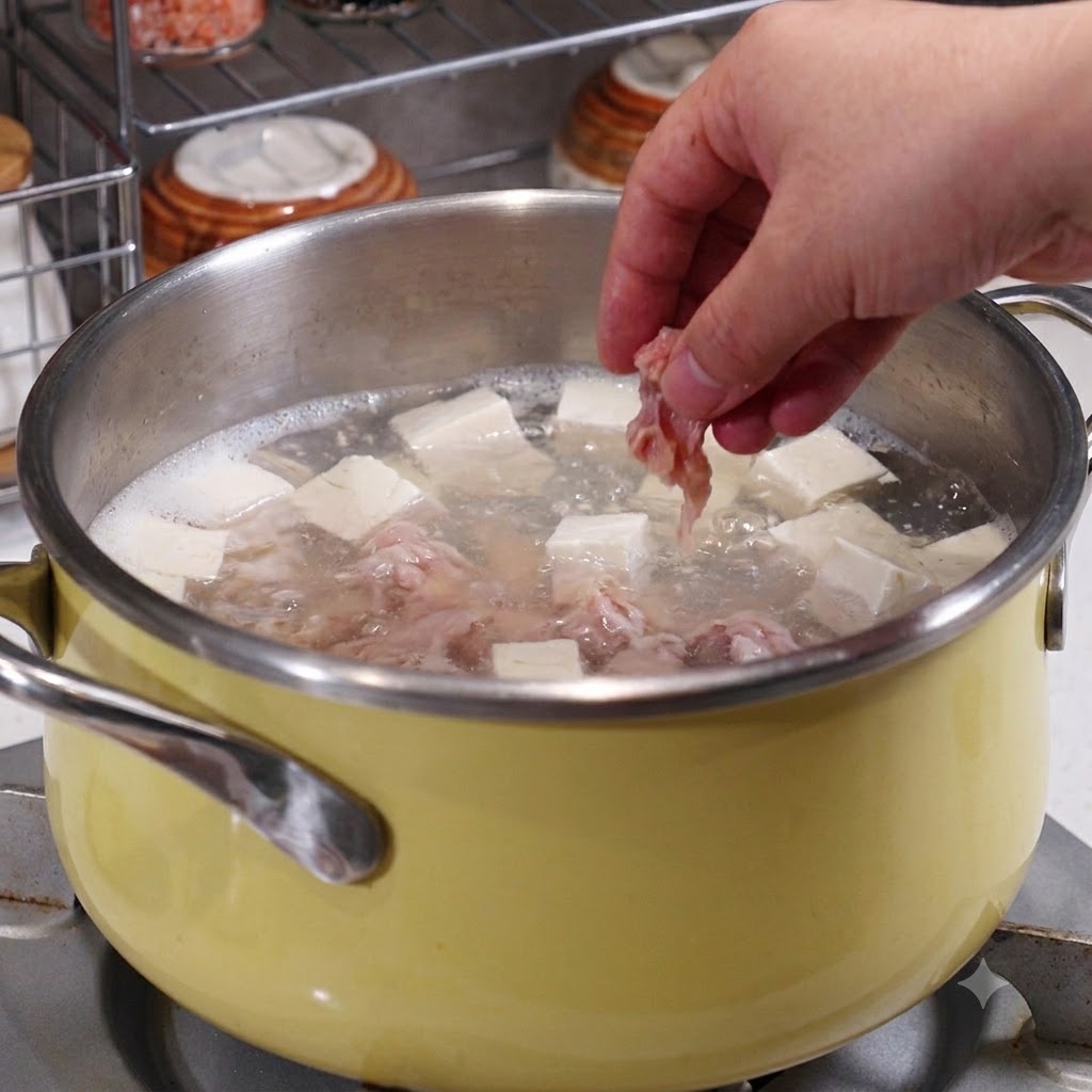 沸騰したスープ、豆腐、魚介の入った鍋に、下味をつけた豚肉のスライスを手で投入しているところ。