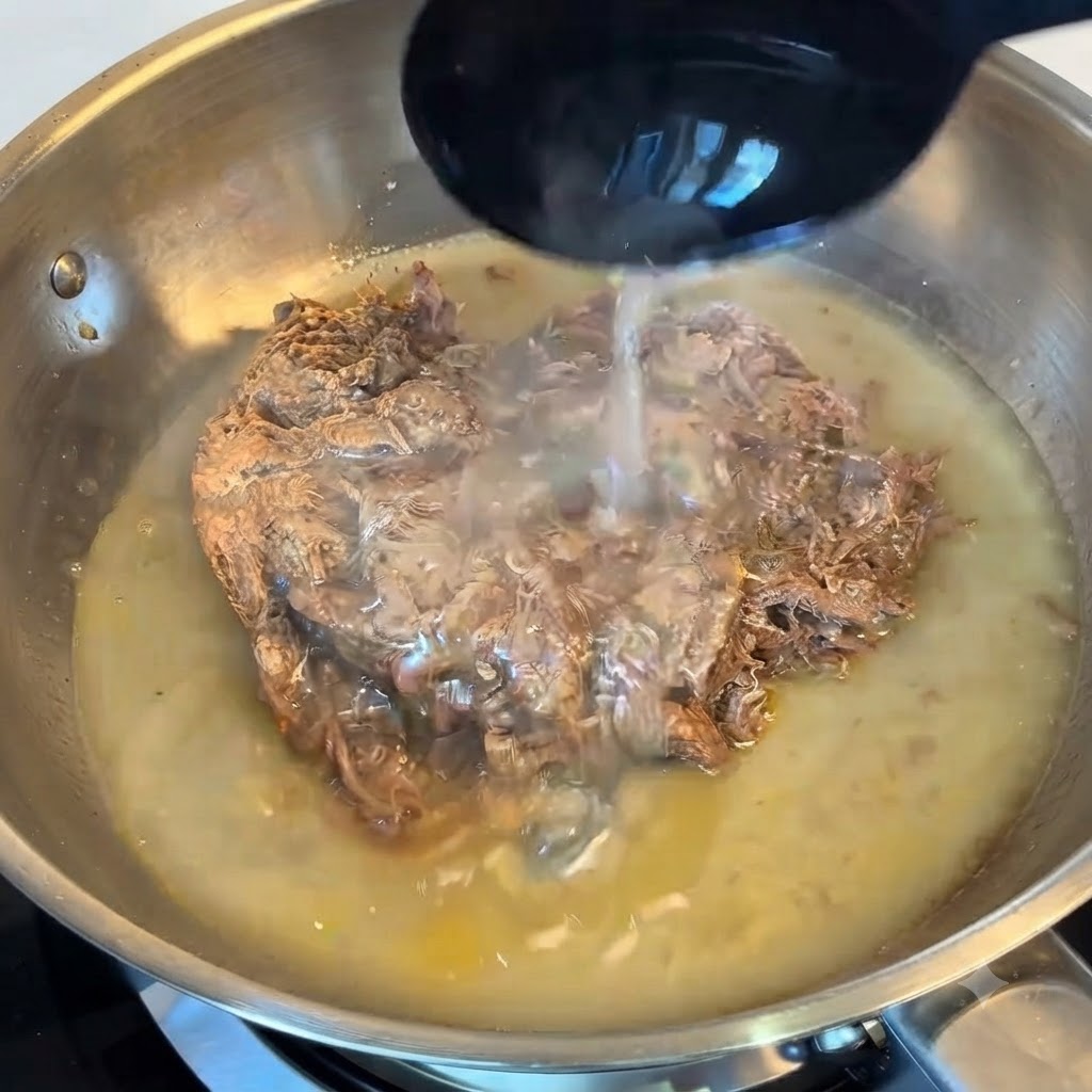 ステンレス製のフライパンの中で、お玉を使ってほぐし牛肉の上にパスタの茹で汁を注いでいるところ。