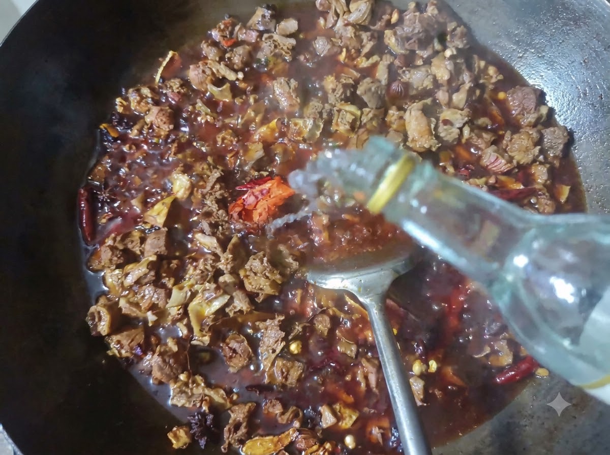 煮込んでいる牛肉とスパイスが入った中華鍋に、ボトルから透明な白酒が注がれている様子。