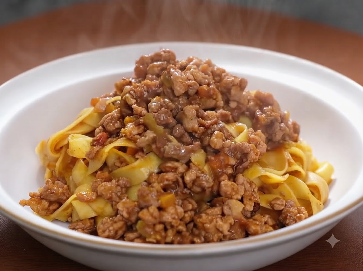 調理中のフライパンで、きつね色に炒めた肉と野菜の混合物にトマトペーストを馴染ませている様子。