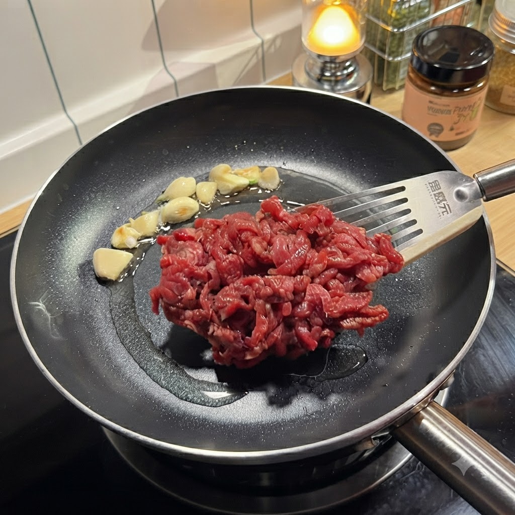 下味をつけた牛肉を、にんにくを炒めた熱いフライパンにヘラで入れている様子。