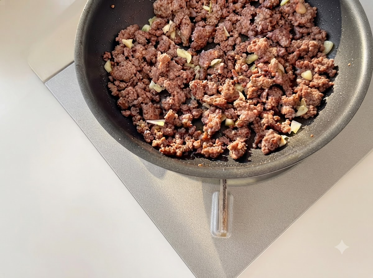 炒めた牛ひき肉と一緒に、みじん切りにしたにんにくと角切りのトマトをフライパンで炒めている様子