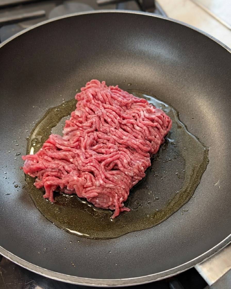 油をひいたフライパンに、生の牛ひき肉、玉ねぎ、にんにくが入っている様子。