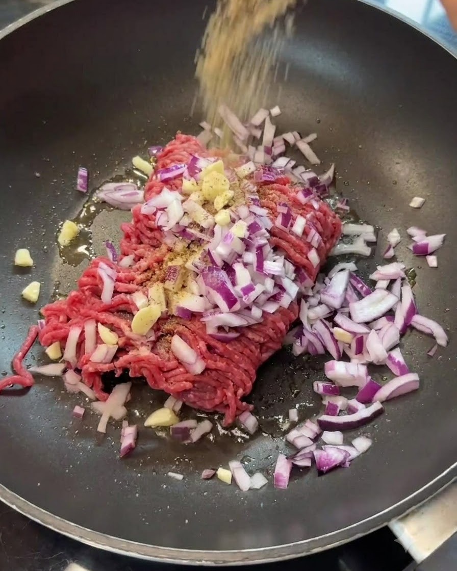 フライパンの中の牛ひき肉と玉ねぎにスパイスを振りかけている様子。