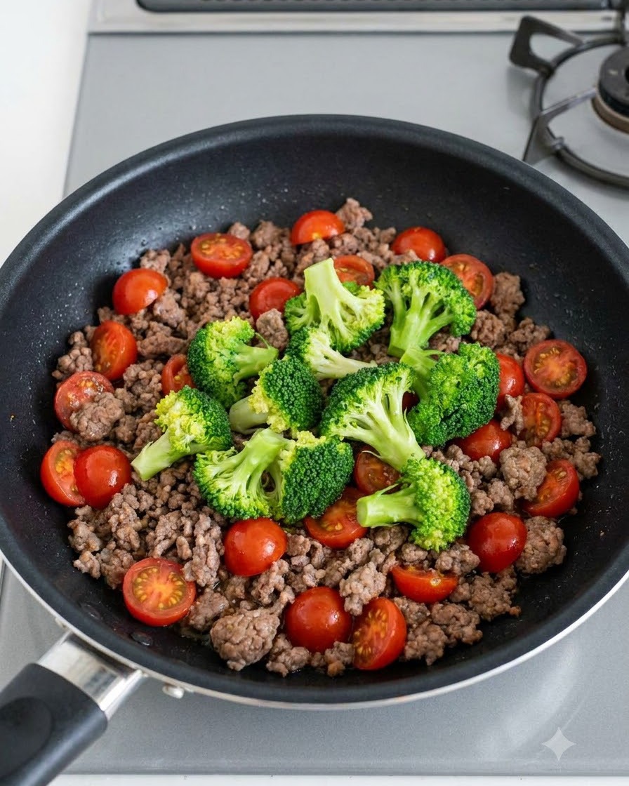 炒めた牛ひき肉の上に、緑のブロッコリーと鮮やかな赤いミニトマトが散らばっているフライパン。