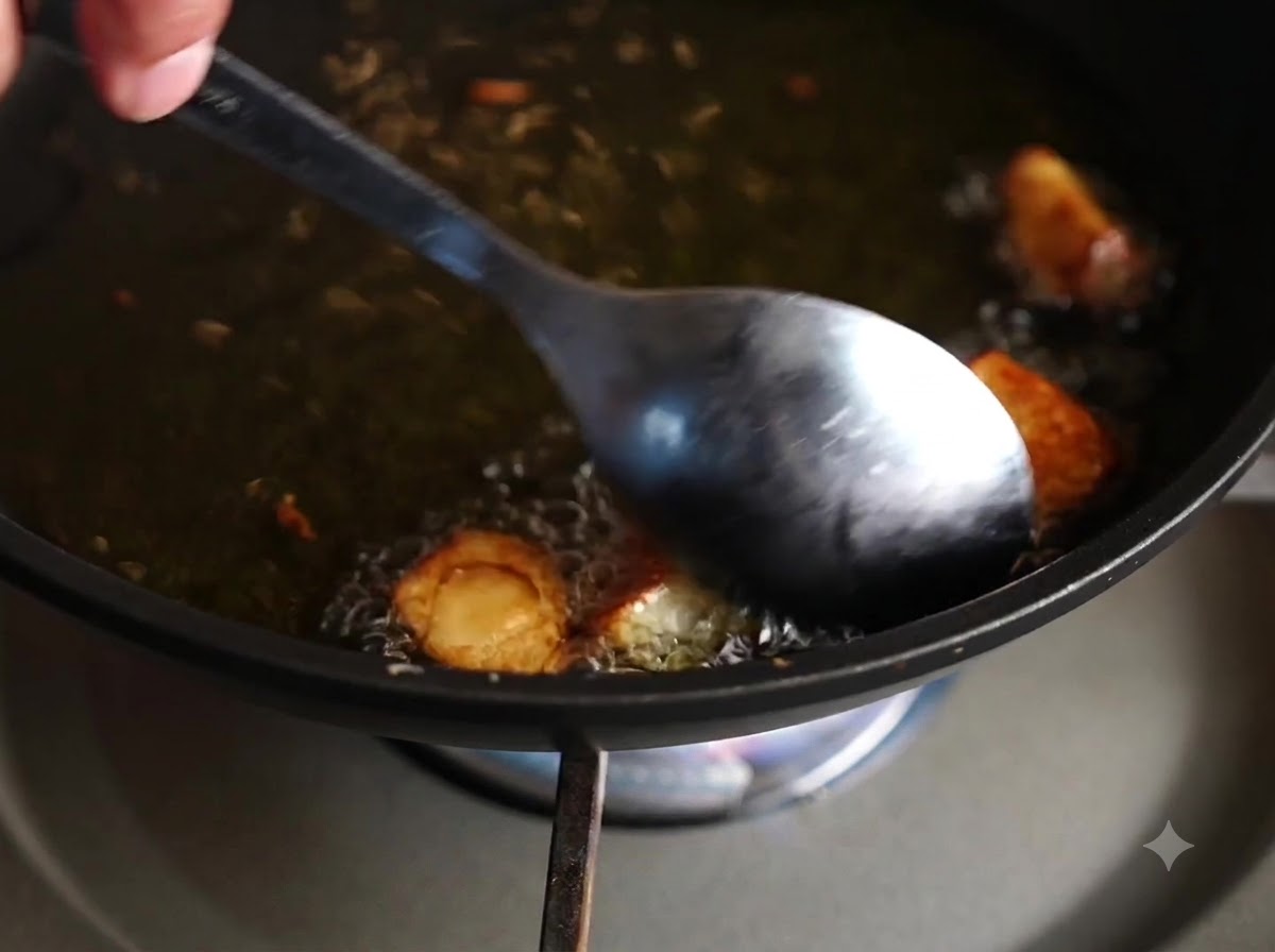 熱したオイルの中で揚がっているニンニクの cloves をスプーンで混ぜて返している様子。