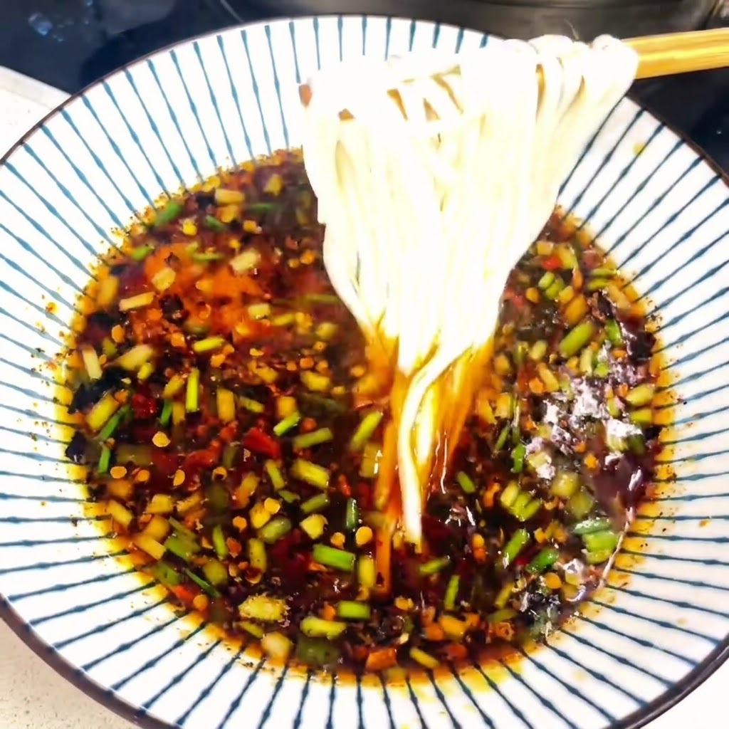 味付けされたスープの入った器から、箸で茹で上がった白い麺を持ち上げているところ。