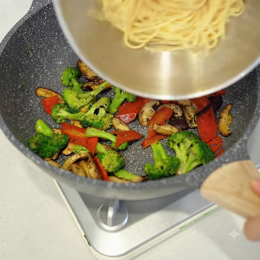 ボウルから炒めた野菜の入ったフライパンへ、茹で上がったスパゲッティが加えられている様子。