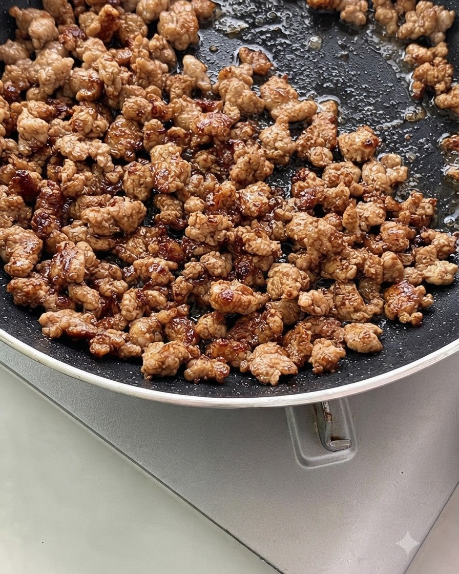 フライパンの中で、ひき肉に刻んだ青ねぎとにんにくが混ざって香ばしく炒められているところ。