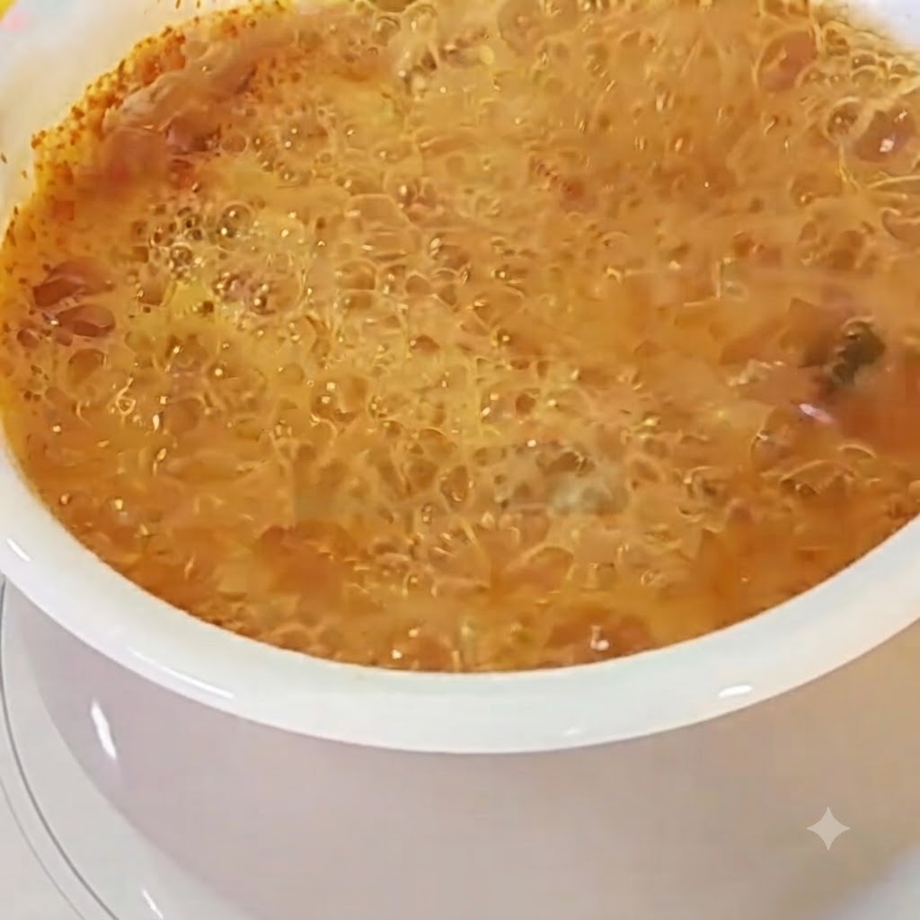 ぐつぐつと煮える赤みがかったラーメンのスープに割り入れられた卵。