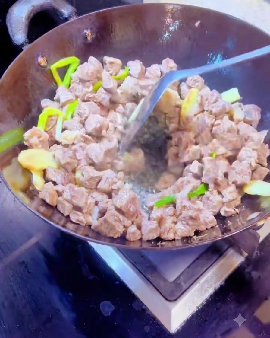 金属製のヘラを使い、熱した中華鍋の中で乾燥スパイスと牛肉の角切りを一緒に混ぜ合わせているところ。