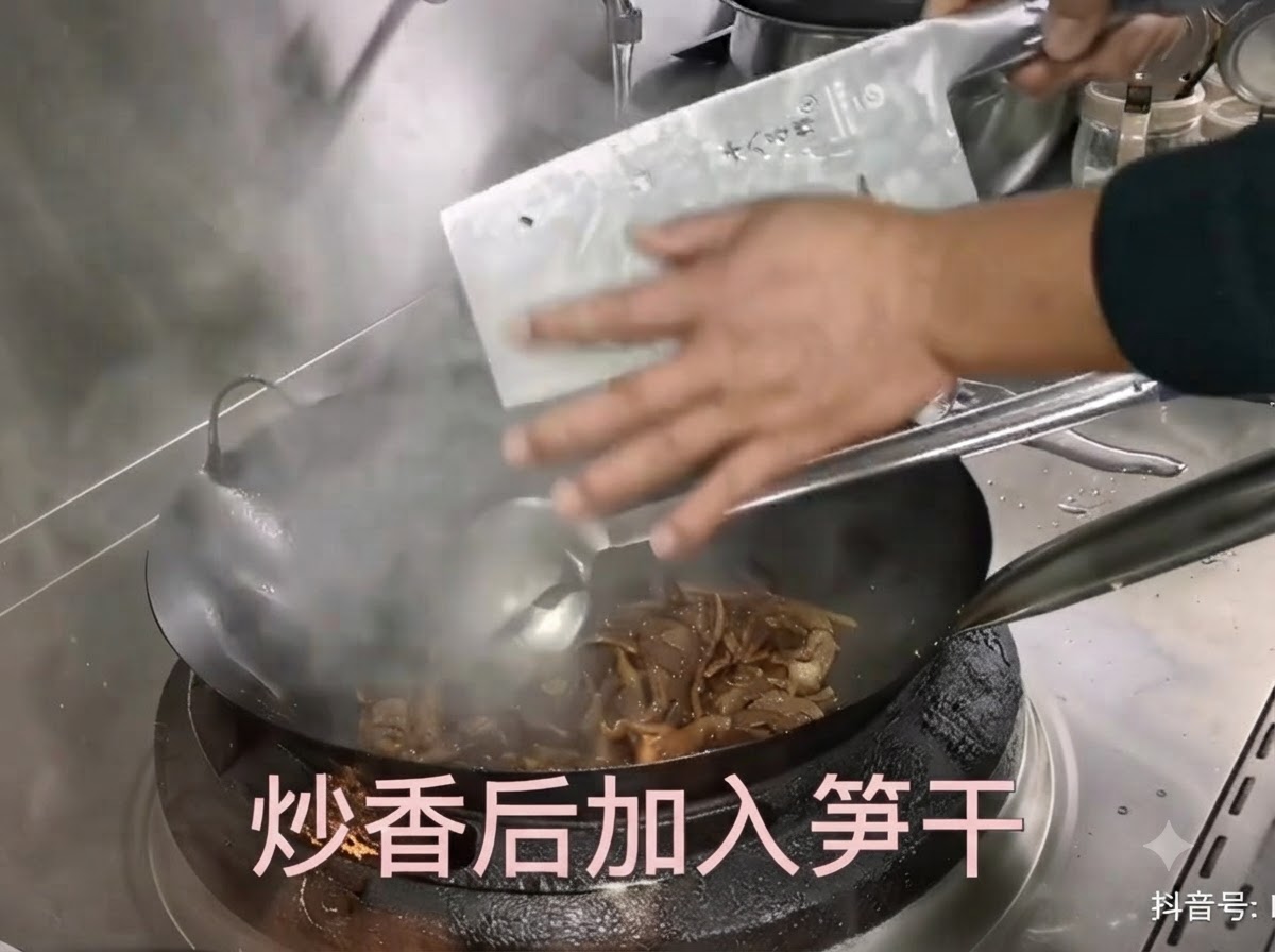 菜刀将处理好的干笋拨入正在翻炒肉丝的热锅中。