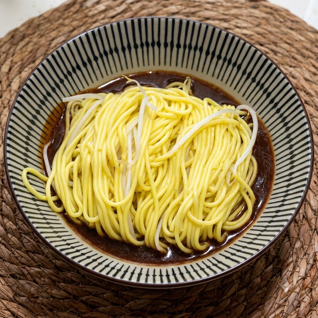 濃厚で濃い茶色のタレが入った柄のある陶器のボウルの中に、茹でたての黄色い麺が入っている様子。