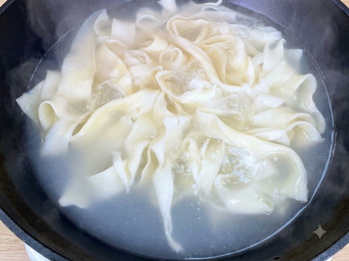 平打ち麺と一緒にチンゲン菜を鍋で茹でている様子。