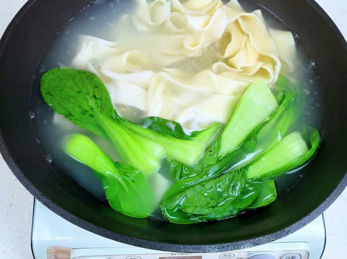 箸を使って茹で上がった麺とチンゲン菜をお湯から引き上げている様子。