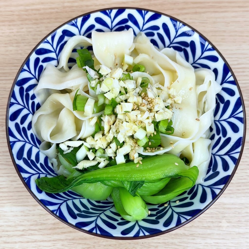 ボウルのにんにくと麺の上に白ごまとスパイスが振りかけられている様子。