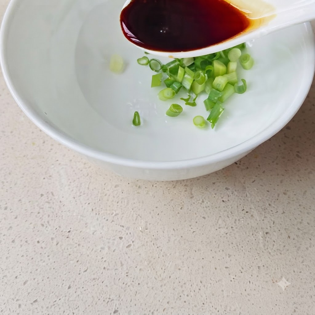 刻みネギが入った白い器に、白いスプーンで醤油を注いでいる様子