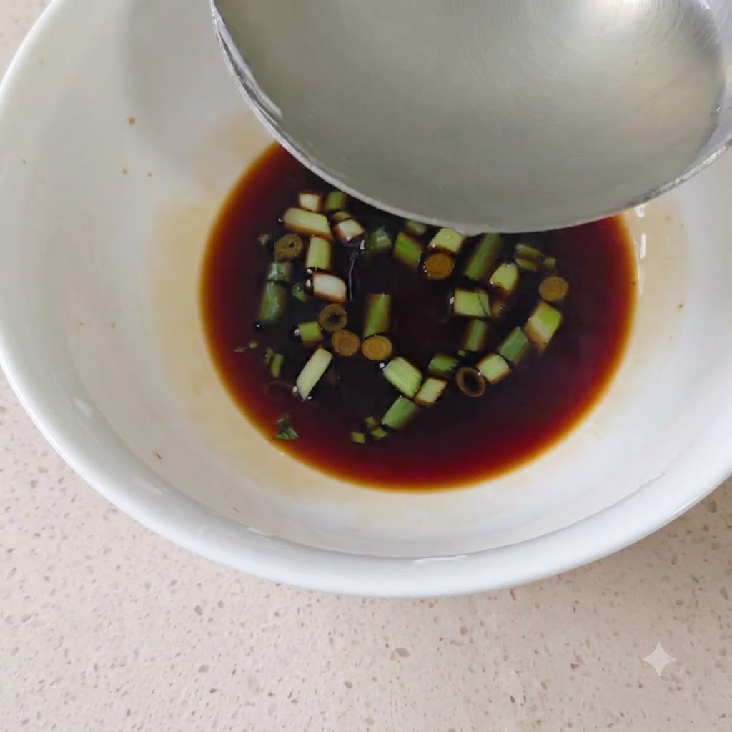 醤油と刻みネギが入った白い器に、お玉で熱湯を注いでいる様子