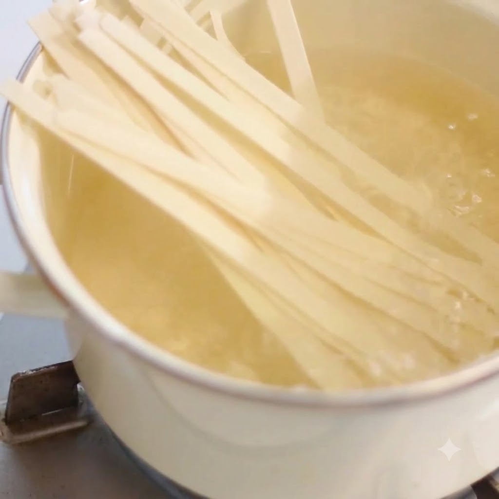 コンロの上の熱いお湯が沸騰した鍋の中で茹でられている平打ち麺。