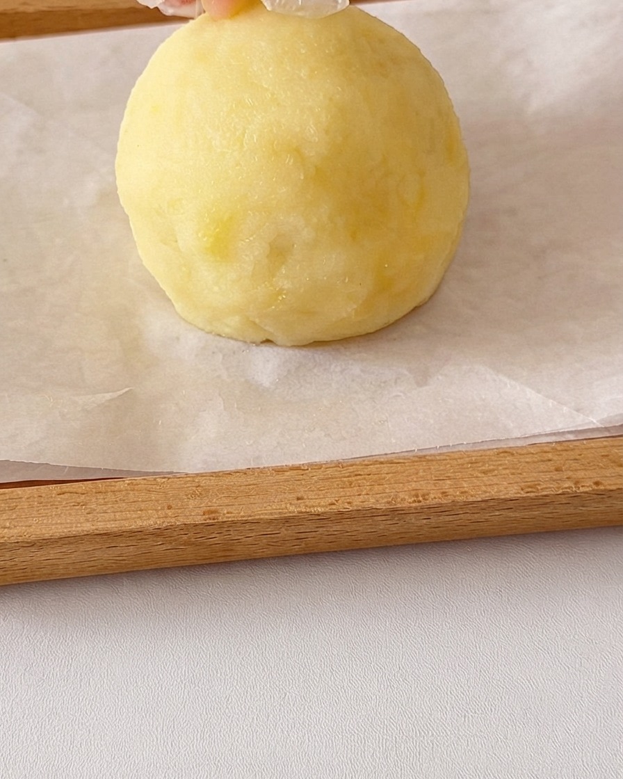 手で滑らかなマッシュポテトの丸いボールが形作られ、上に耳用の小さなポテト片が追加されている様子。