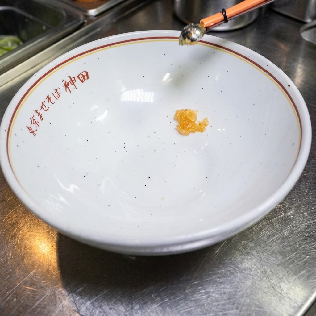 日本語の文字が書かれた白い丼の底に少量のタレが入っている様子。