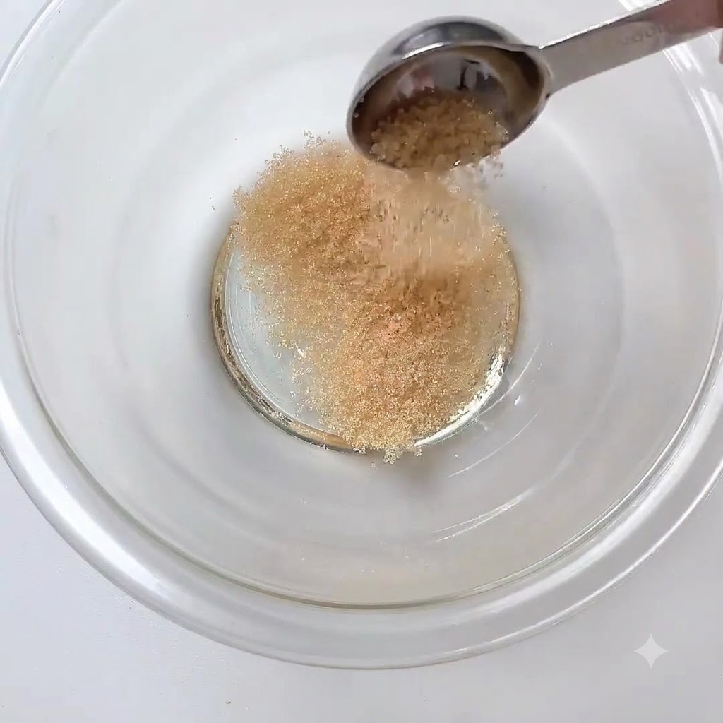 ボウルに入れられた砂糖に、スプーン一杯のすり白ごまが加えられている様子。