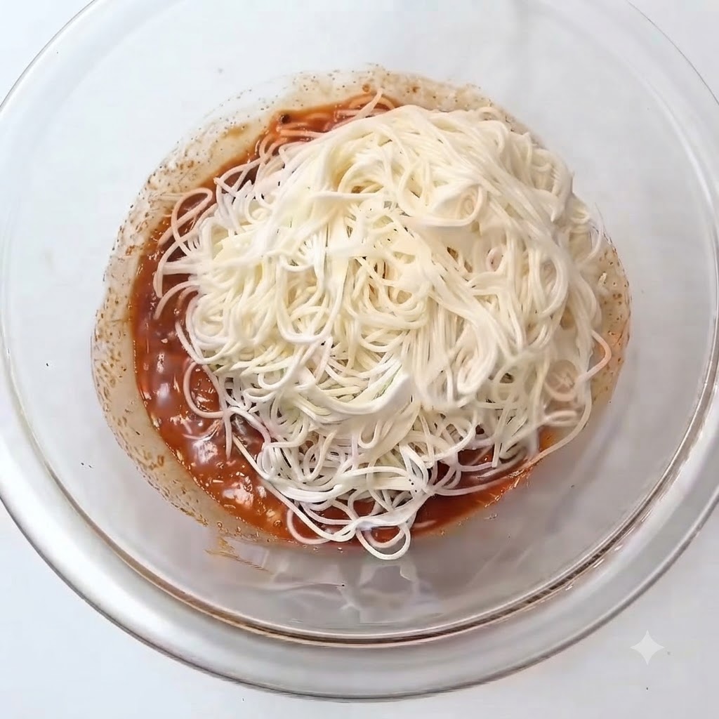 ガラスボウルの中の赤みがかったタレの上に、茹でた白いそうめんの山が置かれている様子。