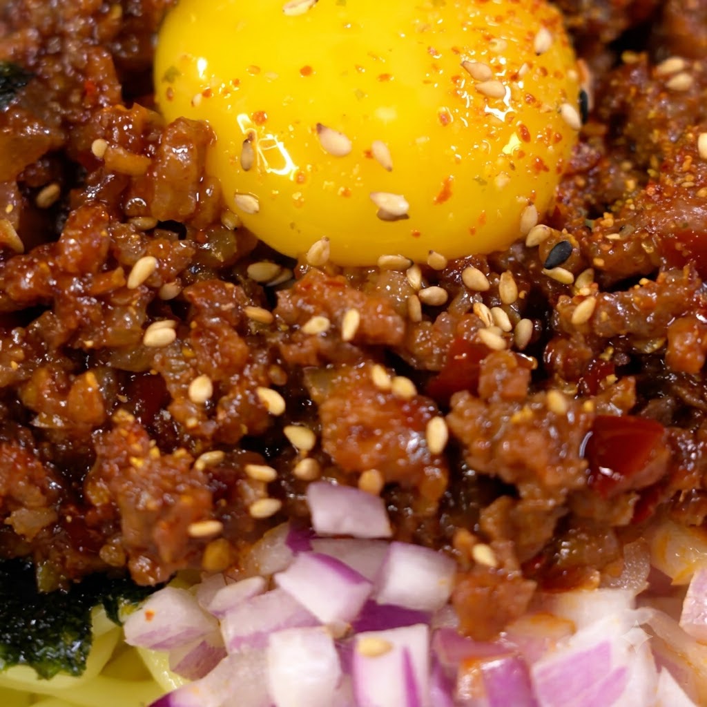 こんがり焼けたひき肉にソースを流し入れて混ぜ合わせている様子