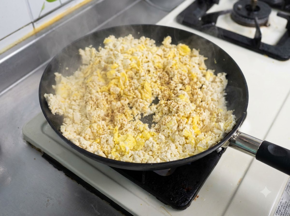 炒り卵と豆腐の混合物が入ったフライパンに調味料がふりかけられ、炒められている様子。