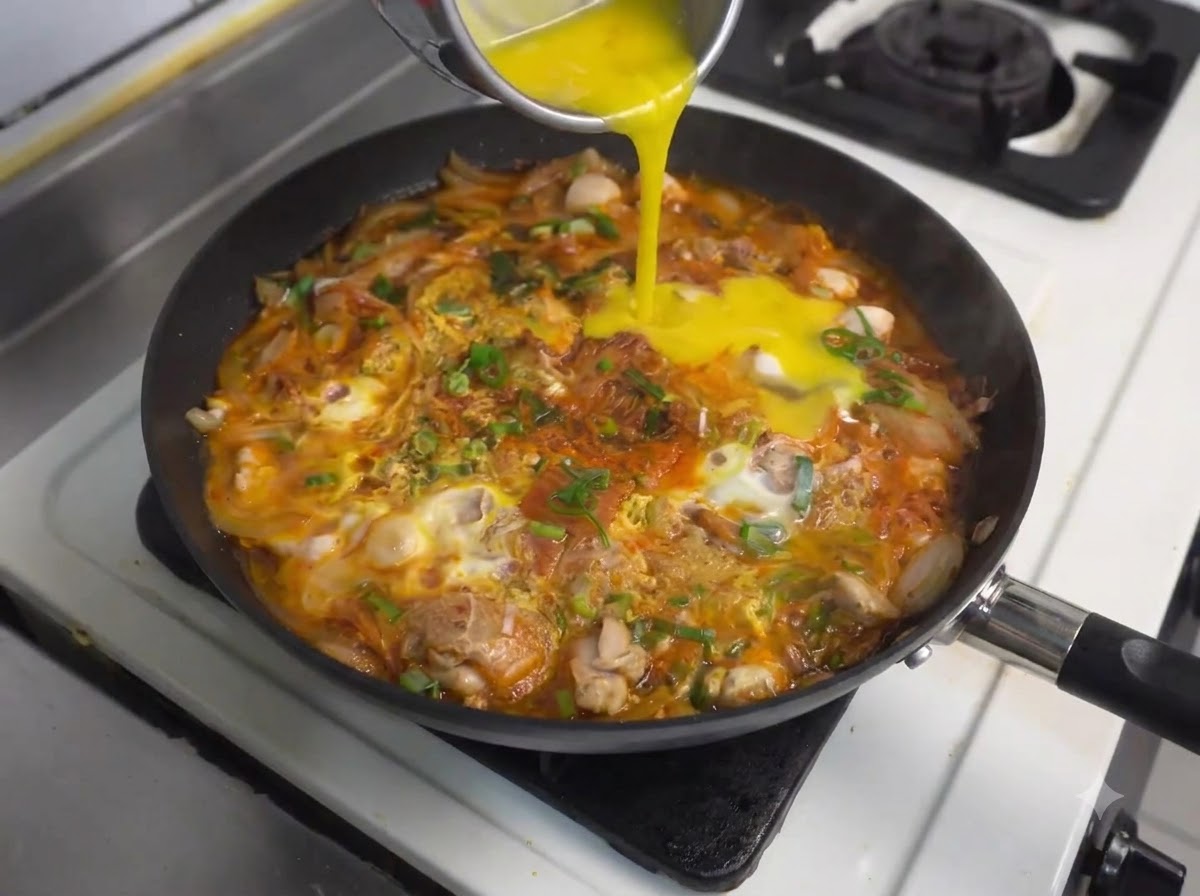 鶏肉とキムチが入った煮込み鍋に追加の溶き卵が容器から注がれている様子。