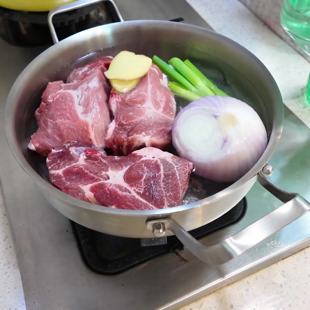 豚肉、玉ねぎ、生姜、小ねぎ、スパイスが入った鍋に水を注いでいる様子。