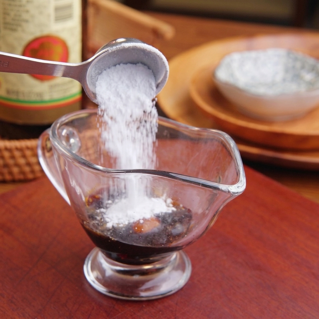 醤油の入った透明な計量カップに、砂糖や液体の調味料を加えている様子。
