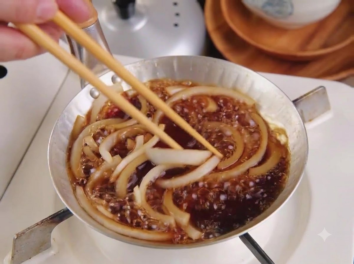 煮立っている玉ねぎとタレの上に、切った豚カツを菜箸でのせている様子。