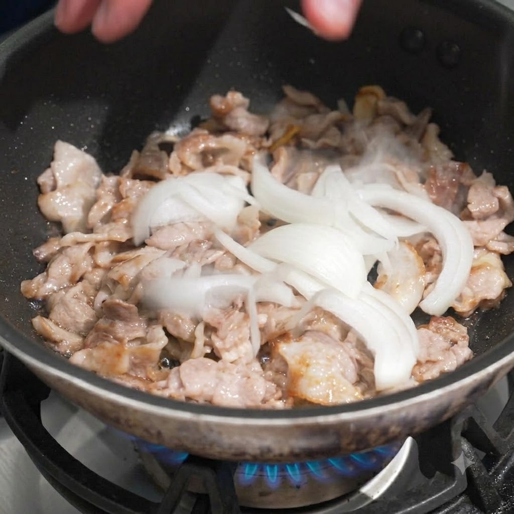 炒めた豚肉の入ったフライパンに、スライスした玉ねぎを手で加えている様子