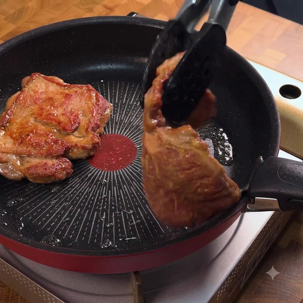 トングを使ってフライパンの中で黄金色に焼けたポークチャップを裏返している様子