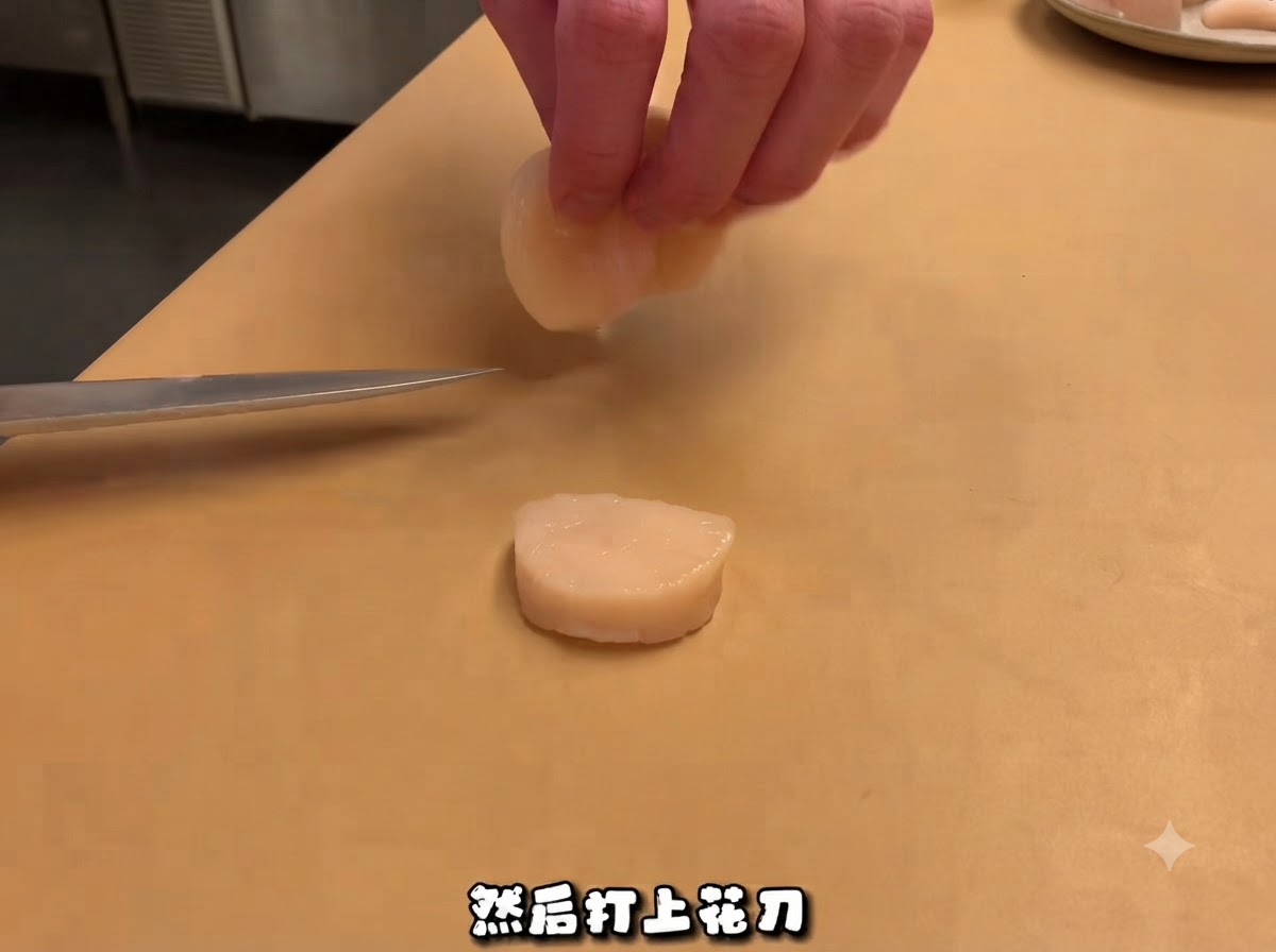 まな板の上に置かれたスライスされたホタテのそばにシェフナイフが置かれ、上部のパーツを手で持っている様子。