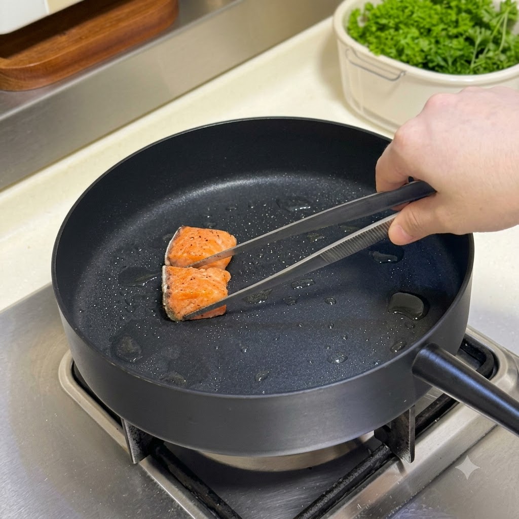 熱したフライパンの中で、トングを使って下味をつけたサーモンを返している様子。