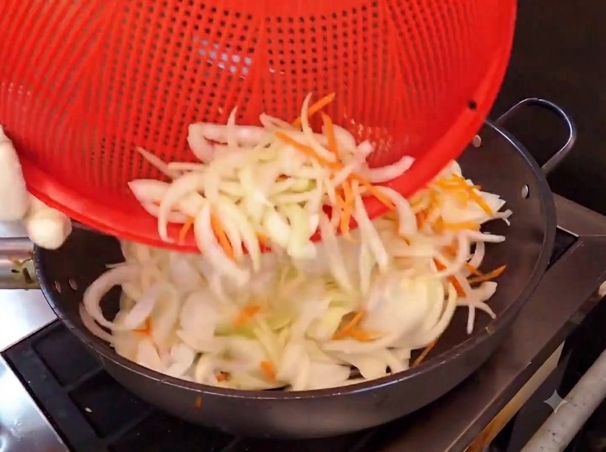 切った玉ねぎとにんじんを熱した中華鍋に入れて炒めている様子。