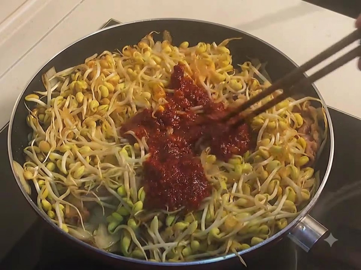 フライパンの中で、豆もやしと牛肉にドロッとした濃い赤色のソースを箸で絡めている様子。
