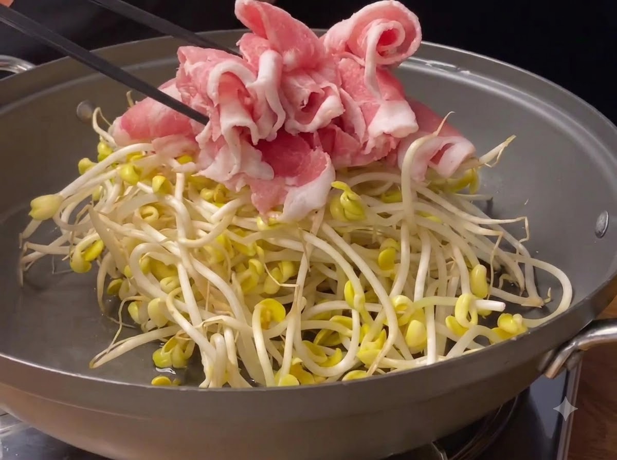 調理用鍋の中の新鮮な大豆もやしの上に置かれる、薄切りのピンク色の豚肉ロール。