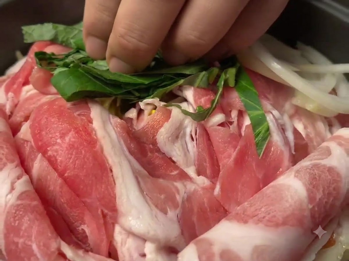 鍋の中の生豚肉の上に散らされる、刻んだ緑色のエゴマの葉。