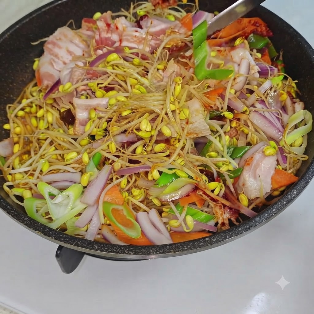 熱せられたフライパンの中で、調理器具がもやし、豚バラ肉、野菜を混ぜ合わせている様子。