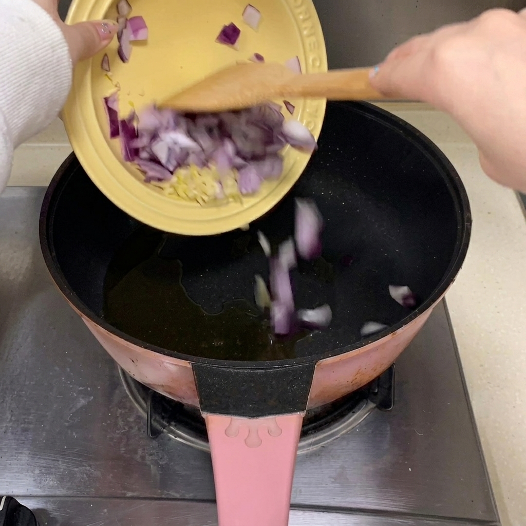 熱した調理油を入れたフライパンに、みじん切りにしたにんにくと赤玉ねぎを入れている様子。