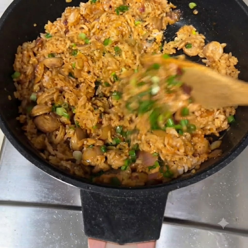 フライパンの中で木べらで炒めご飯を混ぜ合わせ、上に青ねぎを散らしている様子。