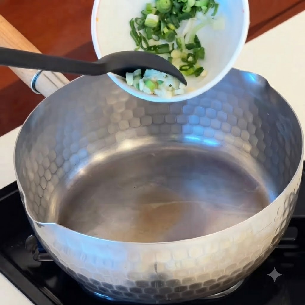 スライスしたにんにく、赤いキムチ、ソーセージをボウルから熱した鍋に入れているところ。
