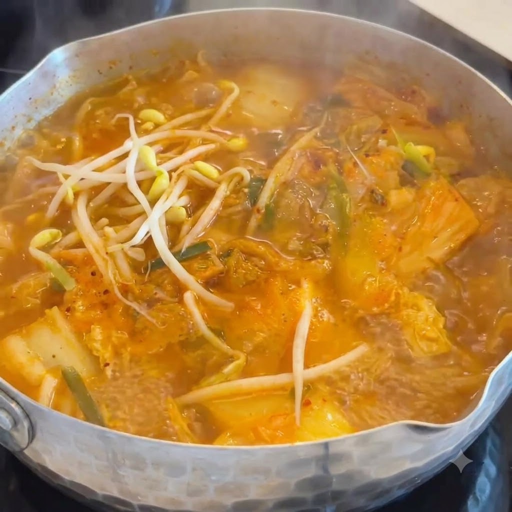 キムチとソーセージのオレンジ色のスープが煮立つ鍋に、白い豆もやしを入れている様子。