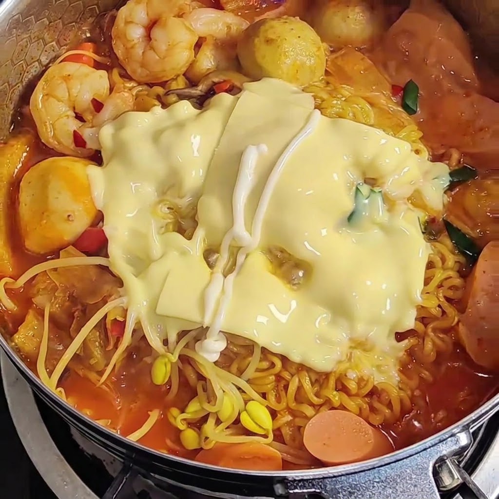 ラーメンの上のとろけたチーズにマヨネーズをジグザグにかけている様子