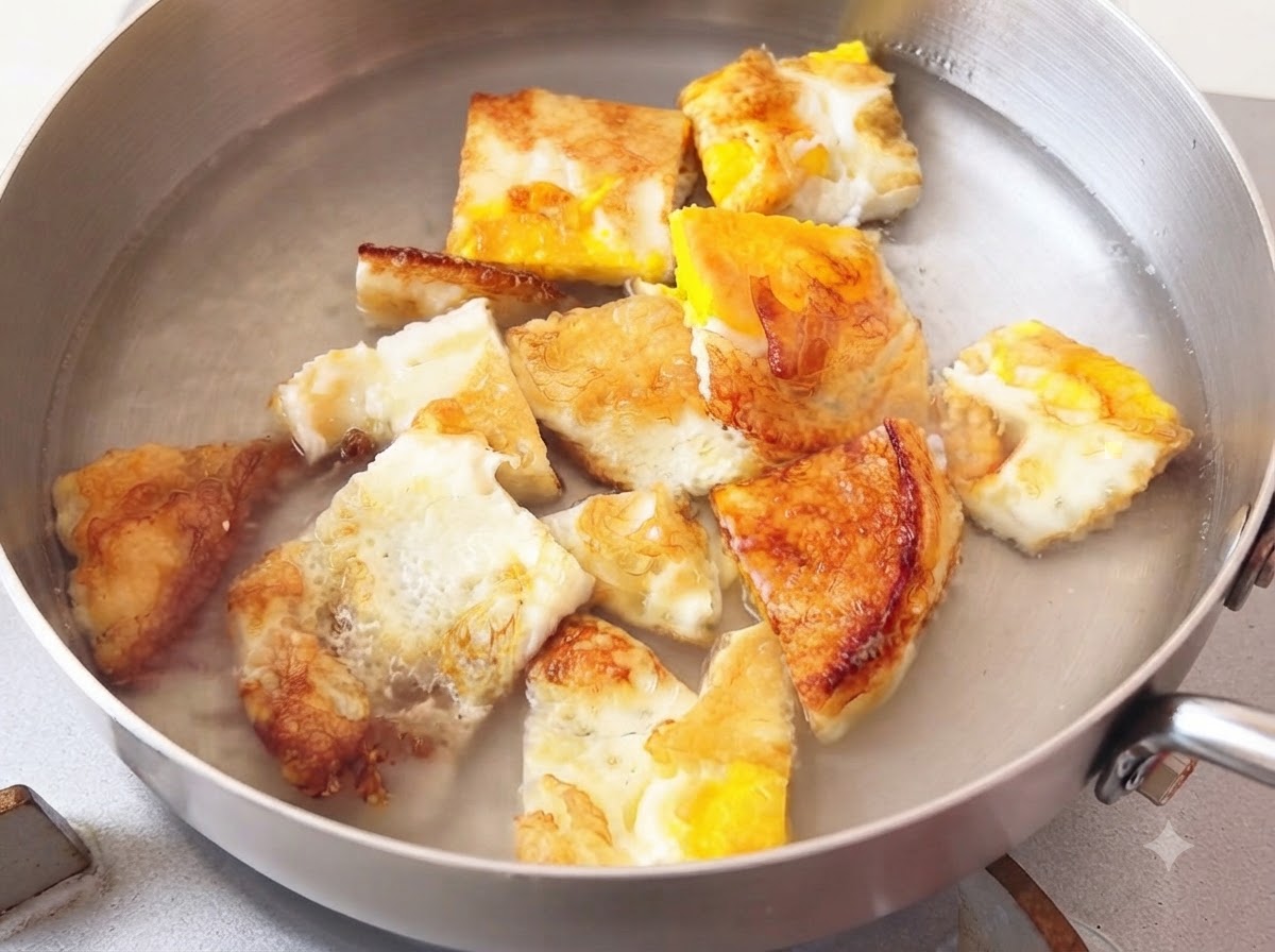 焼き卵の入った金属製の調理鍋に、熱湯を注ぎ入れている様子。