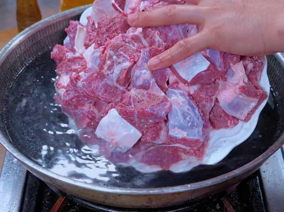 水を入れた鍋に、水に浸した牛肉の塊を入れて下茹でしている様子。